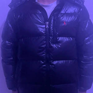 jacka från Ralph Lauren - Säljer en svart dunjacka från Ralph Lauren med huva och dragkedja framtill. Jackan har använts bara den här vintern och behöver säljas eftersom jag ska köpa ny. Model är 175 cm. Pris kan diskuteras vid snabb affär. 