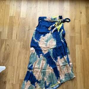 Färgglad omlottkjol från & Other Stories - Säljer en omlottkljol från & Other Stories med batikmönster i blått, beige och gult. Kjolen har knytband i och är i siden!