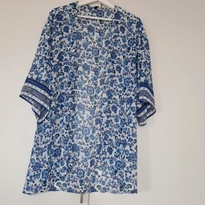 Blommig blå och vit tröja från H&M - Säljer en luftig tröja, utan knäppning, från H&M med blått blommönster på vit botten. Tröjan har trekvartsärm med dekorativa ränder vid ärmsluten och en rak, avslappnad passform. Perfekt för varma dagar eller som strandplagg.