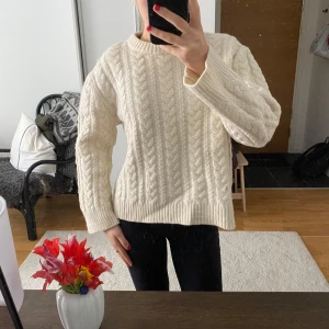 Vit kabel stickad tröja - Säljer en krämvit stickad tröja med klassiskt flätmönster. Tröjan har rund halsringning och långa ärmar, perfekt för kyligare dagar. Passformen är normal och materialet känns mjukt och mysigt.