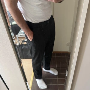 Svarta kostymbyxor herr - Säljer ett par svarta kostymbyxor med normal passform och raka ben. Byxorna har knapp och dragkedja i midjan samt sidfickor. Perfekta för en stilren look och passar till skjorta eller t-shirt.