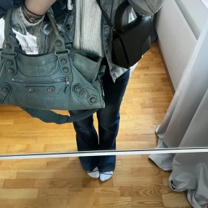 Mörkblå bootcut jeans med knappar - Snygga mörkblå jeans med bootcut-modell och låg midja. Jeansen har dekorativa knappar framtill och lätt slitna detaljer längs benen. Perfekta för en avslappnad och trendig look.