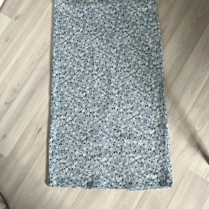 Blommig blå långkjol från Lager 157 - Ljusblå långkjol med små vita blommor och svarta detaljer från Lager 157. Kjolen har en rak passform och en slits baktill för extra rörelsefrihet. Perfekt för dig som gillar en feminin och avslappnad stil.