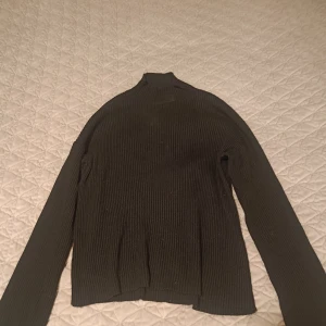 Svart ribbad polotröja - Säljer en svart ribbad polotröja med lång ärm. Tröjan har en hög hals och är tillverkad i ett mjukt, stretchigt material som sitter snyggt på kroppen. Perfekt att styla till olika outfits.