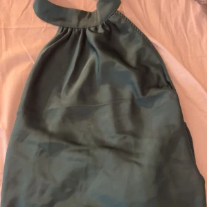 Mörkgrön halterneck blus - Säljer en elegant mörkgrön halterneck blus med hög krage. Blusen har en lös passform och är ärmlös, perfekt för varmare dagar eller att styla