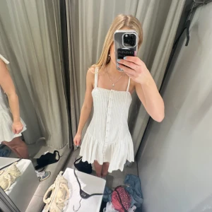 Vit kortklänning med knappar - Supersöt vit kortklänning med smala axelband och knappar framtill. Aldrig använd med prislapp kvar från Zara! Perfekt till sommaren! 