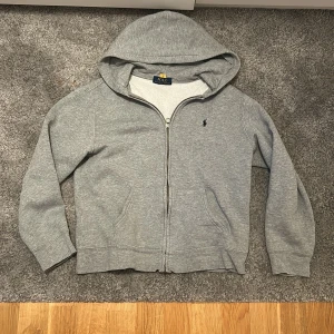 Grå full zip från Ralph lauren i storlek 14-16. - En grå full zip från Ralph lauren. Tröjan är perfekt för en stilren look passar till jeans och joggers. Tröjan är i Ralph laurens egna storlek som är 14-16 som motsvarar 160-170.Nypris 1200 mitt pris 399 priset kan diskuteras.