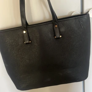 Svart shoppingväska i skinnimitation - Stilren svart shoppingväska med två axelband och enkel design. Väskan är rymlig och passar perfekt för att bära med sig allt man behöver under dagen. 