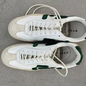 sneakers från Eytys - Säljer ett par vita sneakers från Eytys med gröna detaljer och beige sula helt oanvända typ. Säljer billigt pågrund av har för mycket skor hemma 