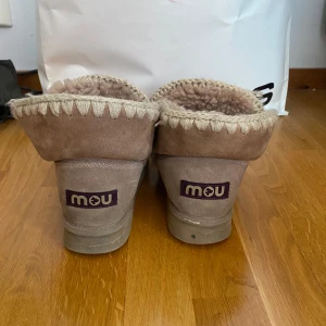 MOU skor - Mysiga beige boots från Mou med grov stickad kant och insida i mjuk fårull. Yttermaterialet är mocka och sulan är platt. Har orginal lådan kvar då de är köpta nya. Nypris: 2 286, 65 kr