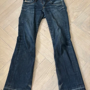 Blå bootcut diesel jeans - Säljer ett par diesel blå bootcut jeans med normal passform. Jeansen har fem fickor, dragkedja och knapp framtill samt snygga slitningar. Köpte för 600kr här på plick. Är i w26 passar xs-s