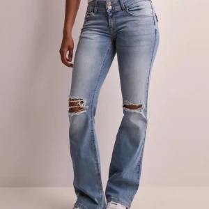 Ljusblå bootcut jeans med hål på knäna - Säljer ett par ljusblå bootcut jeans med slitna hål på båda knäna. Jeansen har normal passform, klassisk femficksdesign och stängs med dragkedja och knapp. Perfekta för en avslappnad och trendig look. Använda men superfina! Nypris 699!