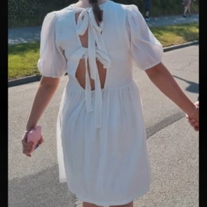 Vit kortklänning med puffärm och knyt i ryggen - Superfin vit klänning med puffärmar och öppen rygg med knytband. Klänningen har en lätt v-ringning framtill och är sydd i ett tunt, strukturerat tyg som känns luftigt. Perfekt för varma dagar och somriga tillfällen. Snygg till studenten❤️Köpt den för 1800 kr och använd 1 gång❤️