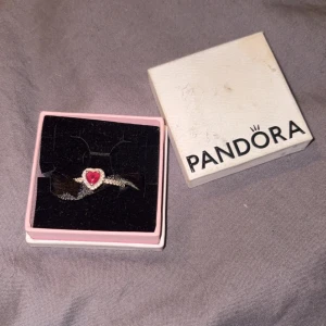 Silverring med rosa hjärta från Pandora - Säljer en söt silverring från Pandora med ett röt hjärta i mitten och små glittriga stenar runt om. Perfekt som present till nån du älskar storlek 52