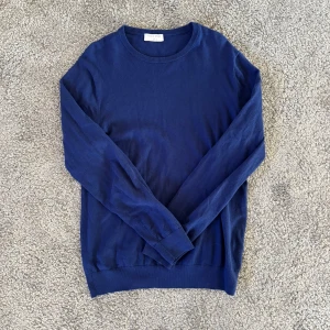 Blå stickad tröja från Tiger of Sweden - Säljer en stilren blå tröja från Tiger of Sweden. Tröjan har rund halsringning och långa ärmar. Perfekt för dig som gillar klassisk och enkel stil. Inga tecken på användning. Hör av dig vid frågor! 