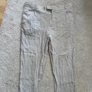 Ljusgråa linnebyxor från Selected Homme - Säljer ett par ljusgråa linnebyxor från Selected Homme. Byxorna har normal passform, dragkedja och knapp i midjan samt diskreta fickor fram. Perfekta för varma dagar och en stilren look.                                                  