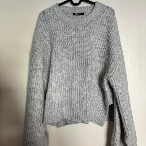 Ljusgrå stickad tröja med slits - Mysig ljusgrå stickad tröja från Gina Tricot med rund halsringning och ribbad struktur. Tröjan har långa ärmar och en något croppad passform, perfekt för lager på lager under kyliga dagar. Slits på sidorna.                Använd fåtal gånger