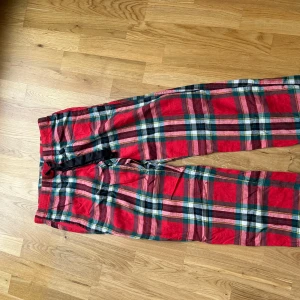 Röd-rutiga pyjamasbyxor från Victoria's Secret - Säljer ett par röd-rutiga pyjamasbyxor från Victoria's Secret med svart dragsko i midjan. Byxorna har elastisk midja och är perfekta för att chilla hemma. Mjukt bomullsmaterial och klassiskt rutigt mönster. Storlek s