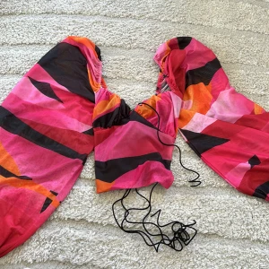 Färgstark tröja med snörning - Säljer en tröja med färgstarkt mönster i rosa, orange och svart. Tröjan har långa ärmar med resår vid handlederna och snörning i midjan. Perfekt för dig som vill sticka ut med en unik look!