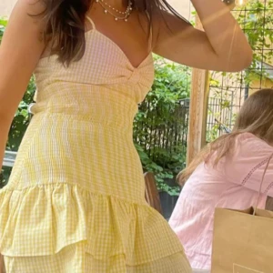 Gul rutig klänning med volang från Zara - Söt gul och vit rutig klänning från Zara med smala axelband, volangkant och rosett man knyter bak till, storlek Xs och använd en gång så den är som ny💗