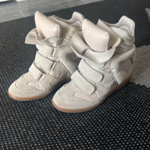 Isabel Marant skor - Äkta Isabel Marant skor i modellen Burt som liknar beckett. Skorna har kilklack. I fint skick förutom lite mörka märken på baksidan av högerskon som syns på andra bilden, en liten fläck på högerskon som syns på sista bilden samt lite smuts som är på undersulan som troligt går bort. Skickas med orginala skokartongen och dustbag. Kan sänka priset vid snabb affär 
