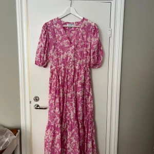 Rosa blommig långklänning från & Other Stories - Säljer en rosa långklänning från & Other Stories med vitt blommigt mönster. Klänningen har v-ringning, knappar framtill och puffade korta ärmar. Perfekt skick då den endast används en enstaka gång!