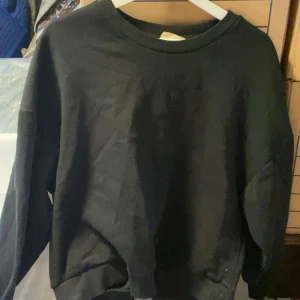 Svart sweatshirt - En klassisk svart sweatshirt med rund halsringning och långa ärmar. Tröjan har en relaxed passform och ribbade muddar vid ärmslut och nederkant. Perfekt basplagg för garderoben.