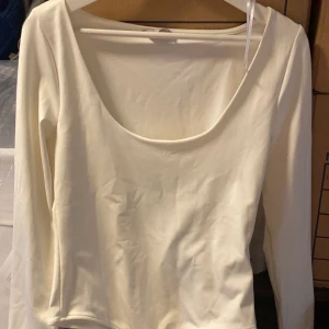 Vit långärmad body med rund ringning - Säljer en stilren vit långärmad body med djup rund ringning. Perfekt att matcha med jeans eller kjol för en enkel och snygg look.