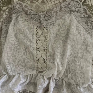 Vit spetslinne  - Säljer ett vitt linne från Bik Bok i spets med blommigt mönster och dekorativ spetskant upptill. Linnet har smala axelband och volang nedtill, perfekt för en somrig look.