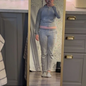 Grå zip-hoodie och byxor från Juicy Couture❤️ - Mjuk och skön grå zip-hoodie från Juicy Couture med huva och fickor framtill. Jackan har långa ärmar, ribbade muddar och en croppad passform. Tillhörande byxor i samma färg och material med fickor fram och back. Perfekt för en avslappnad stil.