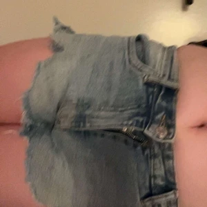 Ljusblå jeansshorts med fransar från Zara - Säljer ett par ljusblå jeansshorts från Zara med råa fransade kanter och klassisk femficksdesign. Shortsen har ganska hög midja och slitna detaljer framtill för en avslappnad look. Perfekta för varma dagar!
