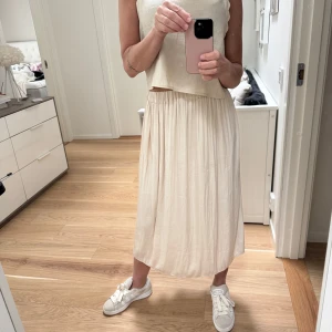 Beige midilång kjol från Gina Tricot, stl S - Säljer en beige midilång kjol från Gina Tricot med resår i midjan. Kjolen har en lätt glansig yta och ett mjukt, följsamt material som ger ett snyggt fall. Perfekt för dig som gillar en enkel och stilren look.