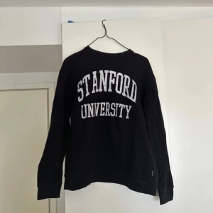 Svart sweatshirt från Stanford University - Svart sweatshirt med vit text 'Stanford University' tryckt på bröstet. Klassisk rund halsringning och långa ärmar. Perfekt för en avslappnad stil.