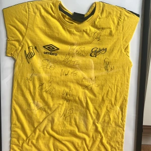 Gul fotbollströja från Elfsborg med autografer - Säljer en gul kortärmad fotbollströja från Elfsborg, tillverkad av Umbro. Tröjan har klubbens logga och flera spelarsignaturer på framsidan. Perfekt för dig som samlar på fotbollsprylar eller är Elfsborg-supporter.