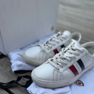Vita sneakers från Moncler  - Säljer ett par vita Moncler sneakers med röd och blå ränder på sidan.        Ny pris: ca 4000.                                            Pris kan diskuteras vid snabb affär             Storlek 41 men passar storlek 42