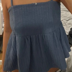 Blå linnetopp med tunna axelband - Säljer en blå linnetopp med tunna axelband och lätt rynkad struktur. Toppen har en luftig och flowy passform, perfekt för varma dagar. Enkel och stilren design som passar till mycket.