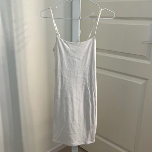 Vit kort klänning med smala axelband från BikBok - Enkel och stilren vit kort klänning från BikBok med smala justerbara axelband. Klänningen har rak passform och är tillverkad i ett mjukt material som känns bekvämt mot huden. Perfekt för varma dagar eller som basplagg i garderoben. Klänningen har en liten fläck på insidan men som inte syns när man har den på sig.🌺