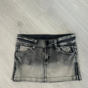 Grå jeanskjol med stjärnfickor från Urban Energy - Säljer en cool grå jeanskjol från Urban Energy med slitna detaljer och dragkedja i sidan. Baksidan har två fickor med broderade stjärnor som ger kjolen en unik look. Perfekt för dig som gillar streetstyle.