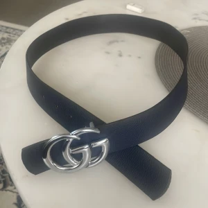 Svart skärp med silverfärgat GG-spänne  - Säljer ett svart bälte  med ett stort, silverfärgat GG-spänne. Bältet är gjort i skinn och har en klassisk, stilren design som passar till många outfits.