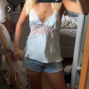 Satinlinne med spetsdetaljer - Säljer ett linne i satin med tunna axelband och v-ringning. Toppen har fina spetsdetaljer i ljusrosa. Perfekt för sommardagar!🩷🩵