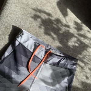 Gråmönstrade träningstights med smart bakficka  - Snygga träningstights i grått med geometriskt mönster och orange snörning i midjan. Tightsen har en praktisk dragkedjeficka baktill och är perfekta för gym eller löpning.