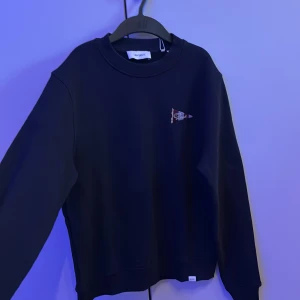 Mörkblå sweatshirt från Les Deux - Säljer en mörkblå sweatshirt från Les Deux i modellen Flag Sweatshirt. Den är använd noll gånger. Original priset är 900kr men säljer den för 550kr. Tröjan har rund halsringning, långa ärmar och en liten flaggdetalj på bröstet. Perfekt för en stilren och enkel look.