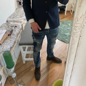 Blå slitna jeans från dondup  - Säljer ett par skit snygga blå dondup jeans med slitningar och tvättade detaljer. Jeansen har raka ben, klassisk femficksdesign och normal passform. Storlek 32 i midjan. 