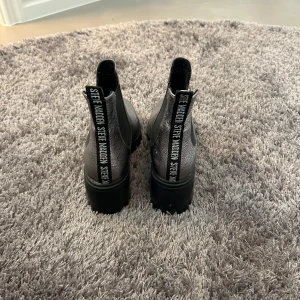 Gråa chelsea boots från Steve Madden - Säljer ett par gråa chelsea boots från Steve Madden med svarta elastiska paneler på sidorna och grov sula. Bak finns en svart rem med vit logotyptext. Perfekta för dig som vill ha en cool och stilren look.