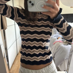 Zickzak tröja  - Säljer en stickad tröja med vågiga ränder i beige och marinblått. Tröjan har lång ärm, rund halsringning och sitter figurnära. Perfekt för dig som gillar retrovibbar och snygga mönster.