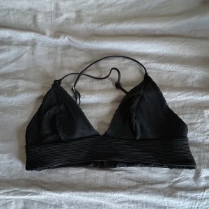 Svart bikinitopp från hm - Säljer svart bikinitopp i riggat mtrrial från hm. Den har justerbara axelband som korsas i ryggen.