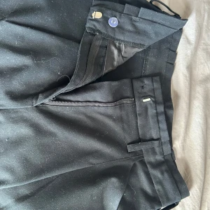 Svarta kostymbyxor från C - Säljer ett par svarta kostymbyxor från C i storlek 38. Byxorna har klassisk passform med dragkedja och knapp framtill samt diskreta bakfickor. Perfekta för en stilren look.