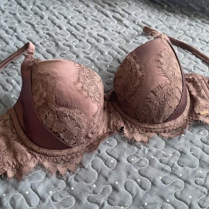 Spets-bh från Hunkemöller - Säljer en brun bh från Hunkemöller med vacker spetsdetalj och vadderade kupor. Bh:n har justerbara axelband och dekorativ spets längs kanterna. Perfekt för dig som vill ha något både snyggt och bekvämt.