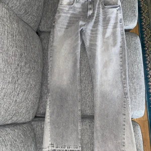 Grå flared jeans från Zara - Säljer ett par grå jeans från Zara med raka ben och snygga råa kanter nertill. Jeansen har klassisk femficksdesign, bälteshällor och knappgylf. Perfekta för en avslappnad och trendig look.