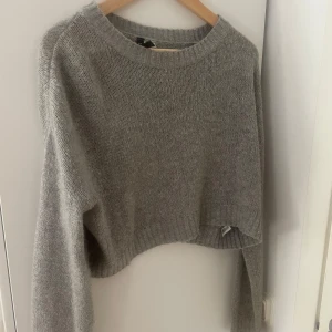 Grå croppad stickad tröja från H&M Divided - Mysig grå stickad tröja från H&M Divided. Modellen är croppad med rund halsringning och långa ärmar. Perfekt för lager-på-lager och passar till både jeans och kjol. Perfekt nu till sommaren!